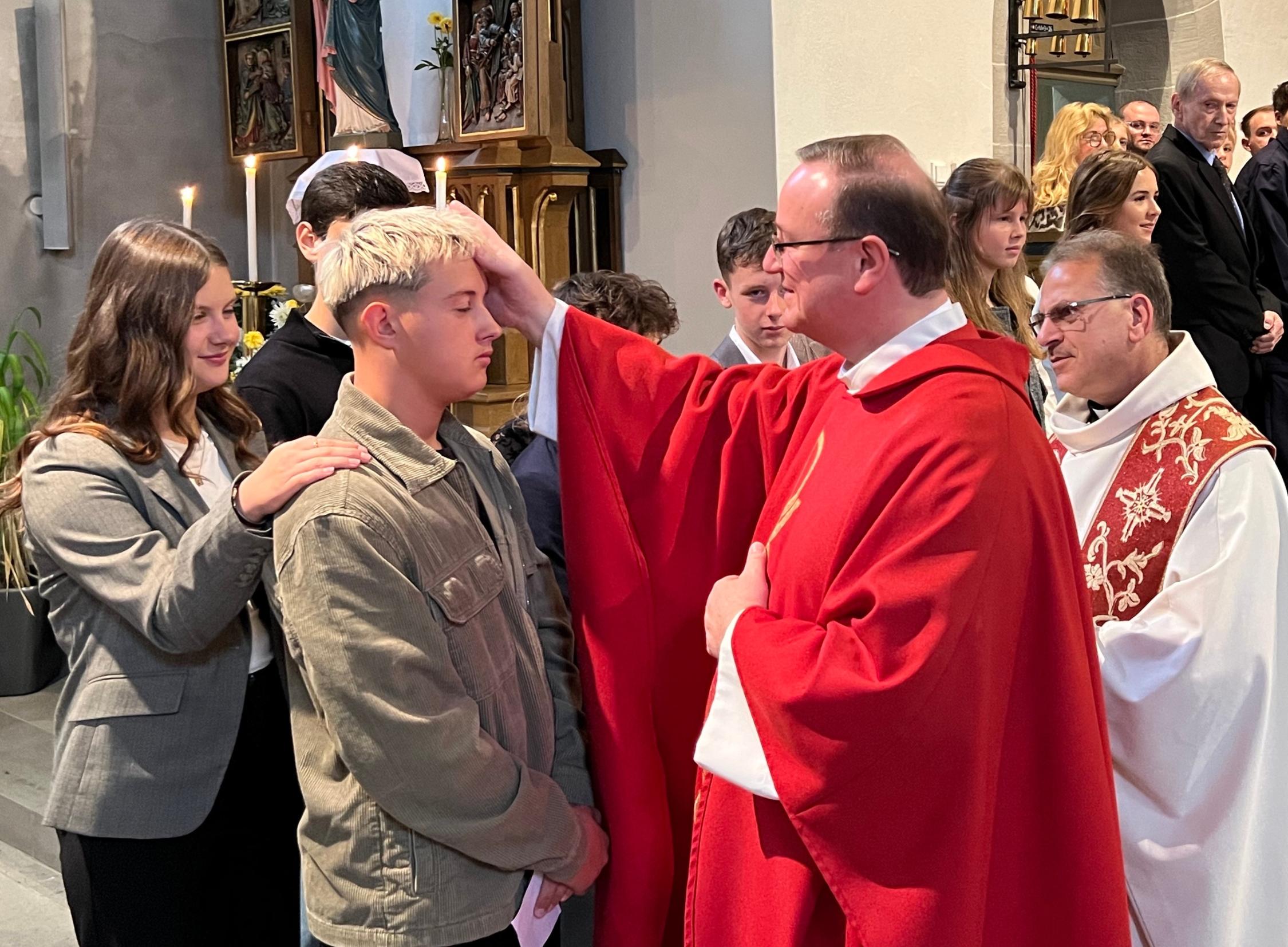 Albert Müller erteilt das Sakrament der Firmung an Vincent Hauck, rechts Pfarrer Richard Reis.